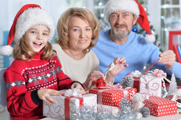 Portrait of grandparents with granddaughter in Santa hats preparing for Christmas at home