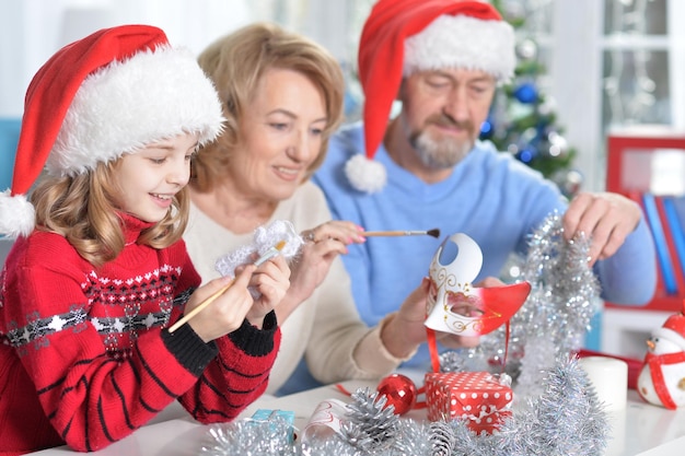 Portrait of grandparents with granddaughter in Santa hats preparing for Christmas at home