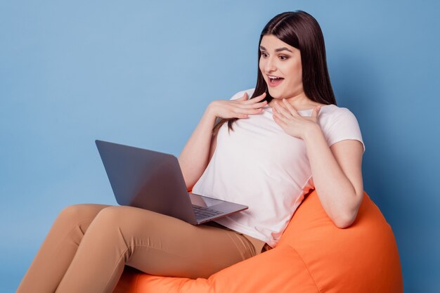 Portrait of grateful happy lovely lady sit beanbag hold computer hands chest on blue background