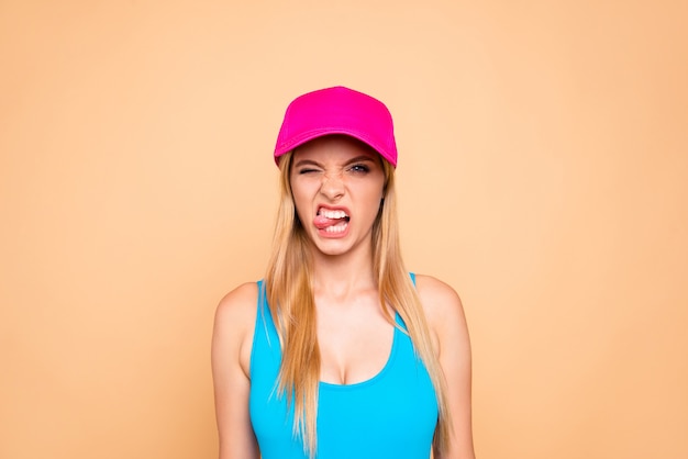 Portrait of grimacing girl showing tongue out isolated on beige