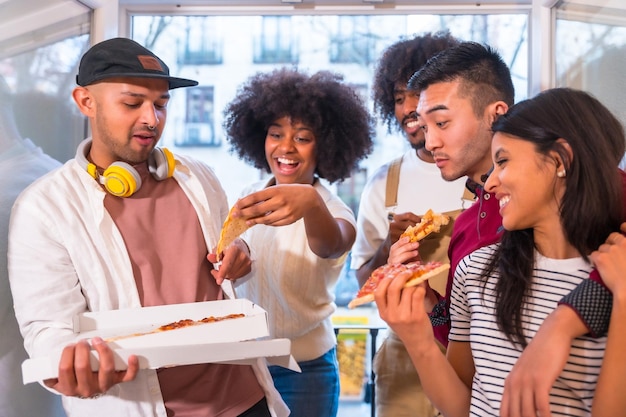 Portrait of a group of friends eating pizza on the terrace at home lunch or dinner lifestyle distributing a delicious pizza from the box