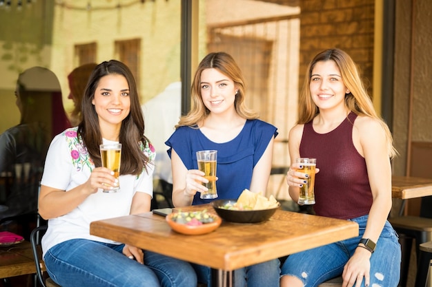 Portrait of a group of three good looking female friends drinking beers in a restaurant