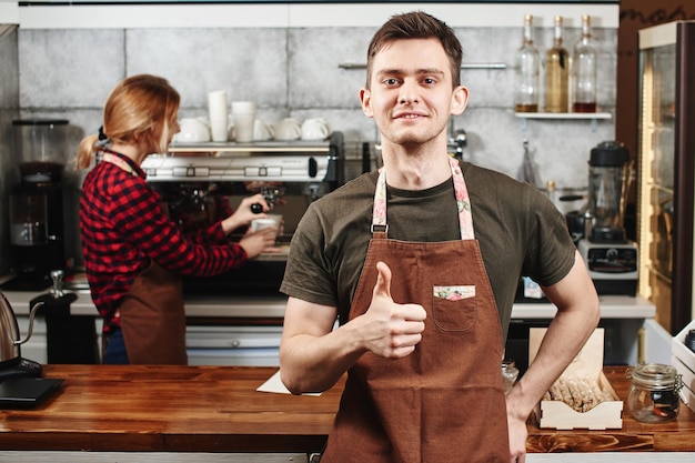 The portrait of the guy baristas at workplace on background of coffee