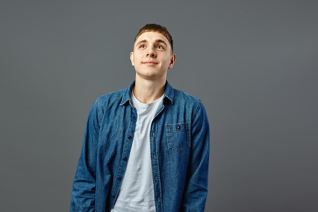 Portrait guy dressed in white t-shirt and a jeans shirt on the gray background in the studio .