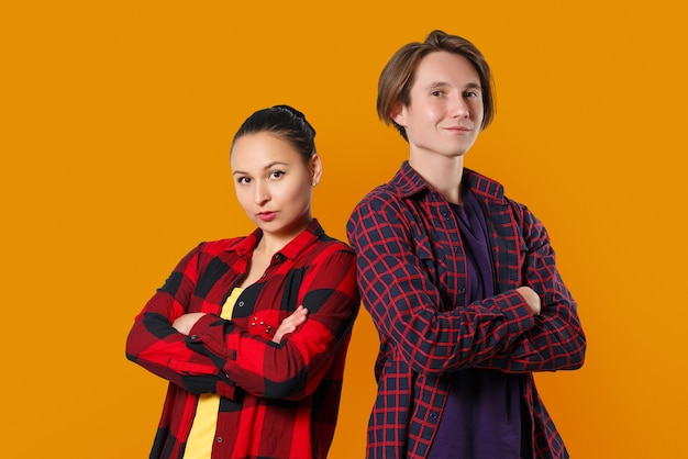 Portrait of a guy and a girl standing side by side, arms crossed in front of them. on bright yellow wall