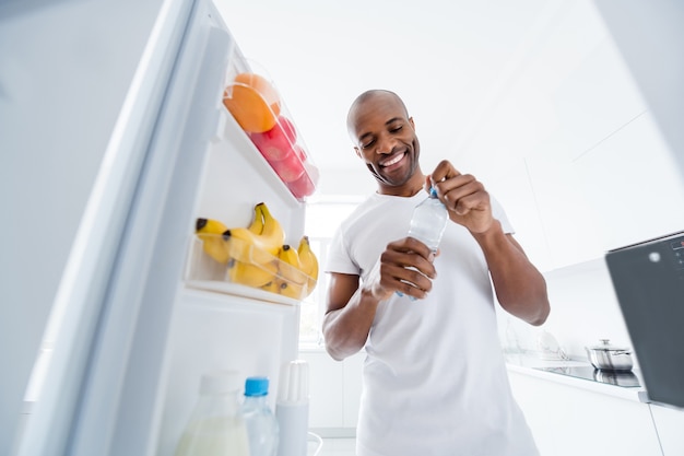 portrait of guy looking in fridge taking snack health care lifestyle regime in kitchen indoors