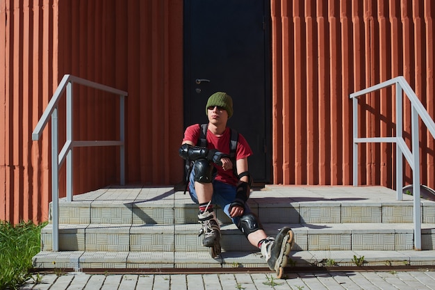 Portrait of a guy in roller skates sitting on the stairs of the building