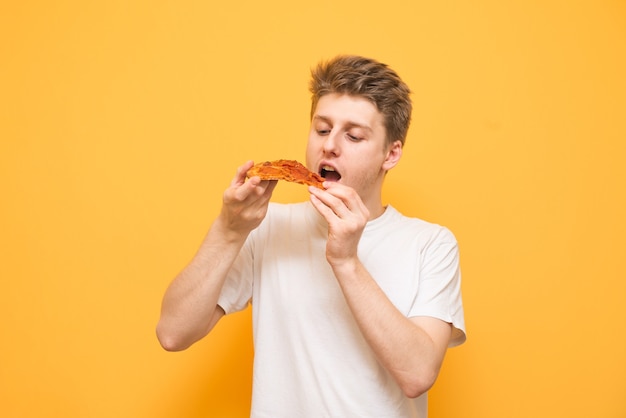 Portrait of a guy in a white T-shirt holds a piece of pizza in his hands