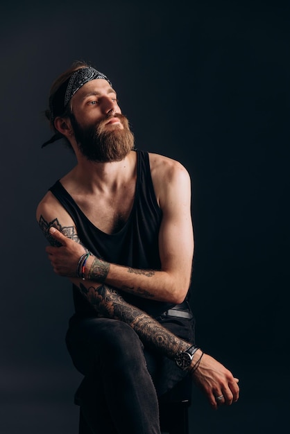 Portrait of a guy with a beard and tattoos on a dark background hipster