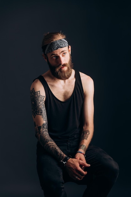 Portrait of a guy with a beard and tattoos on a dark background hipster