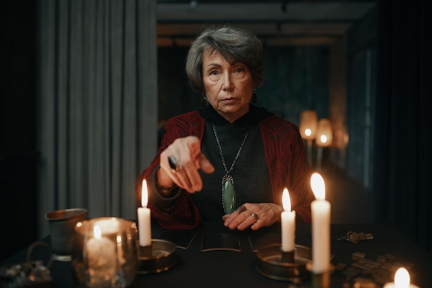 Portrait of gypsy fortune teller with tarot cards on table pointing finger and looking at camera. Online divination session