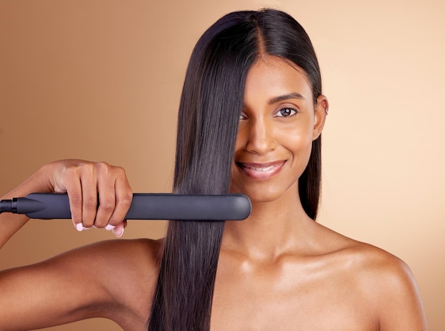 Portrait hair and straightener with a model woman in studio on a beige background for beauty or style Face smile and haircare with happy young person using a flat iron appliance for natural care