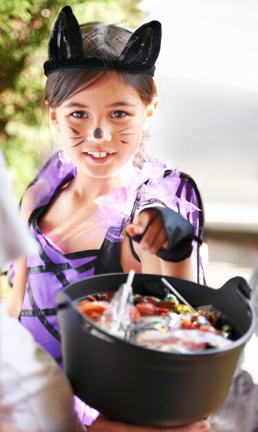 Portrait halloween and girl child with candy in costume for trick or treat tradition on holiday Vacation youth and bucket of sweets with young kid at door of home for fall holiday celebration