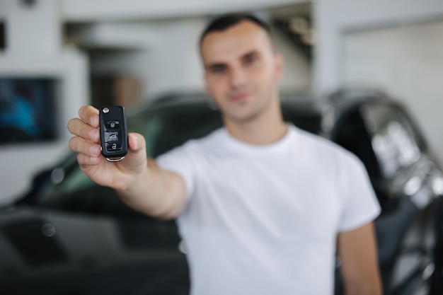 Portrait of handosom man in car showroom man hold keys from her new car keys in focus