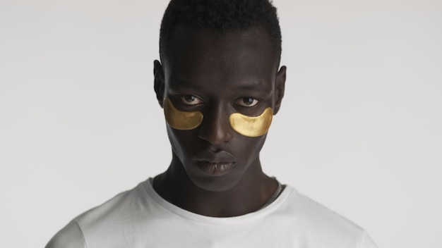 Portrait of handsome African American man with gold eye patches looking serious on camera isolated Facial treatment