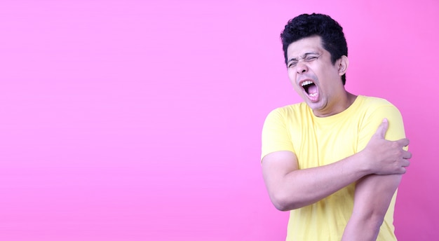 Portrait of A Handsome Asia man, holding his shoulder in pain on pink background in studio