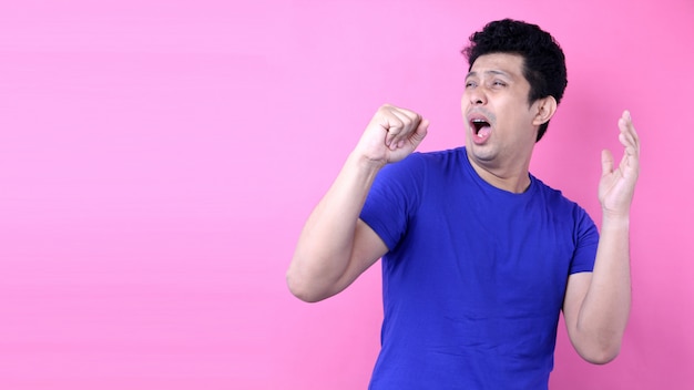 Portrait Handsome Asia man singing loud while standing  on pink background in studio