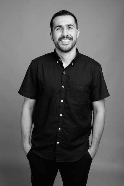 Portrait of handsome bearded Persian man wearing black shirt on gray in black and white