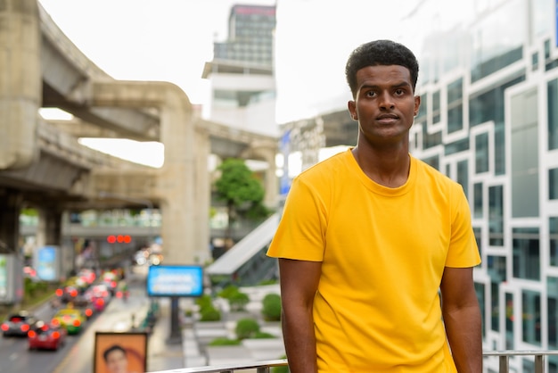 Portrait of handsome black African man wearing yellow t-shirt outdoors in city in Bangkok, Thailand