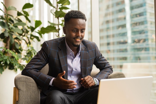 Portrait of handsome black businessman sitting in coffee shop using laptop computer