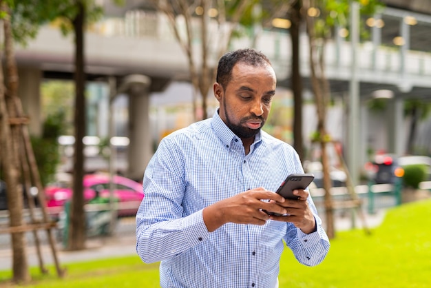 Portrait of handsome black man in city using phone