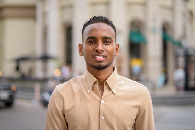 Portrait of handsome black young African businessman wearing casual clothes outdoors in city