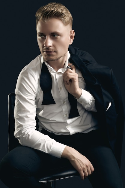 Portrait of handsome blond man in elegant tuxedo and bow tie posing on black  wall