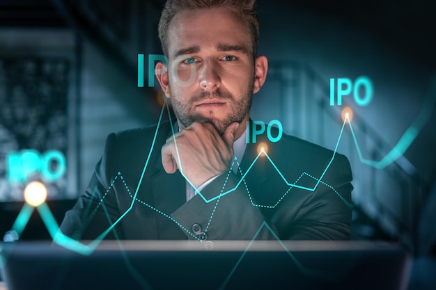 Portrait of handsome businessman in formal suit thinking how to optimize IPO strategy Financial chart hologram over modern office background Go public concept Hand on chin