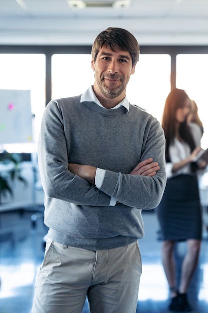 Portrait of handsome businessman is looking at camera while his colleagues are working on coworking place.