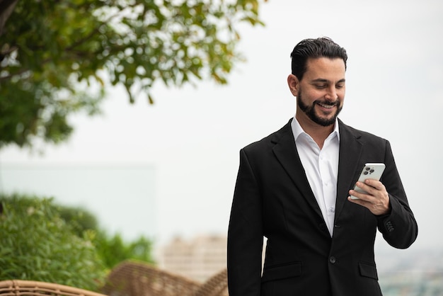 Portrait of handsome businessman outdoors at rooftop using phone