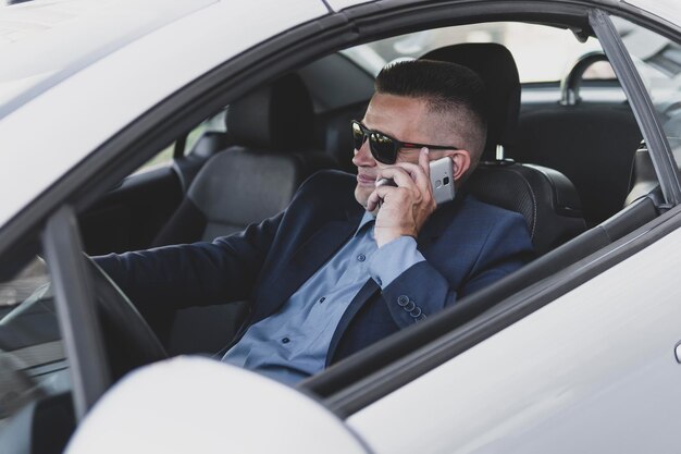 Portrait of handsome businessman speaking by phone sitting in seat of car and smiling happily. driver communicates on smartphone while driving. businessman chatting cheerfully at the wheel