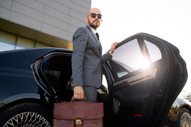 Portrait of a handsome businessman in sunglasses standing near the car outdoors