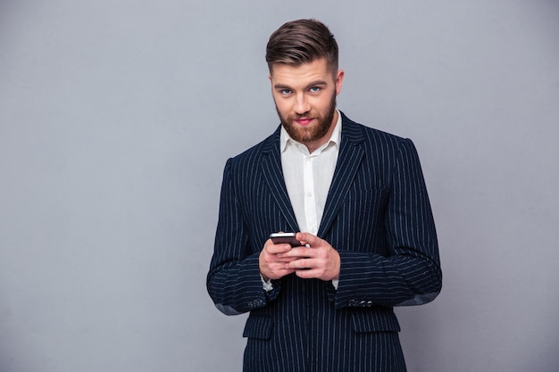 Portrait of a handsome businessman using smartphone over gray wall and looking at camera