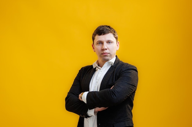 Portrait of handsome businessman with crossing hands standing on yellow studio background and looking at camera