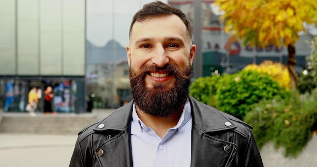 Portrait of the handsome Caucasian young man with long beard standing on the street and smiling.