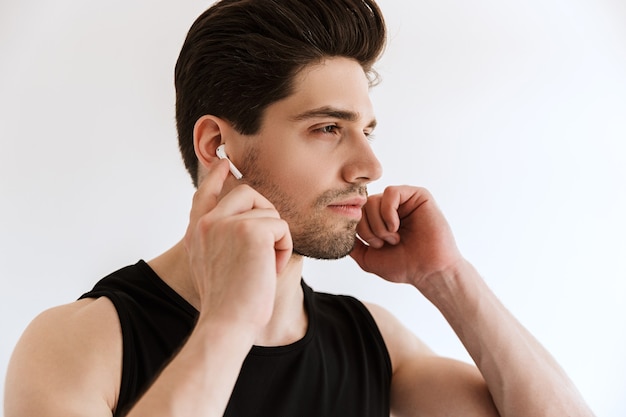 Portrait of a handsome concentrated young sports man isolated over white wall listening music with earphones.