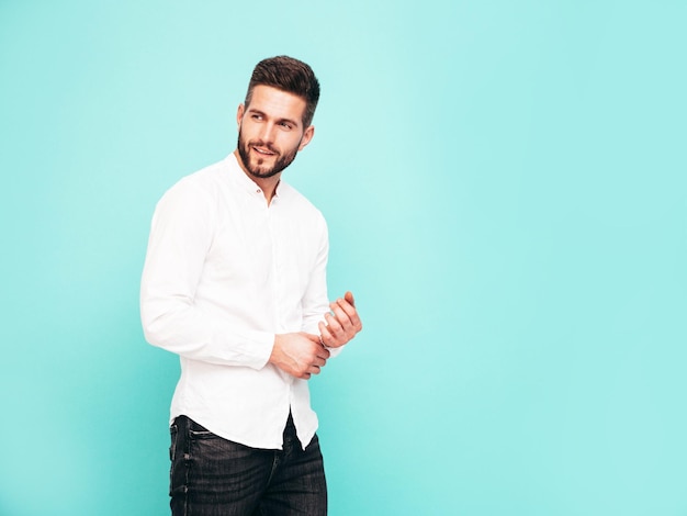 Portrait of handsome confident model Sexy stylish man dressed in white shirt and jeans Fashion hipster male posing near blue wall in studio Isolated