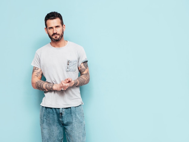 Portrait of handsome confident stylish hipster lambersexual model Sexy man dressed in Tshirt and jeans Fashion male isolated on blue wall in studio