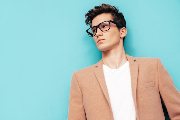 Portrait of handsome confident stylish hipster lambersexual model Sexy modern man dressed in elegant beige suit Fashion male posing in studio near blue wall