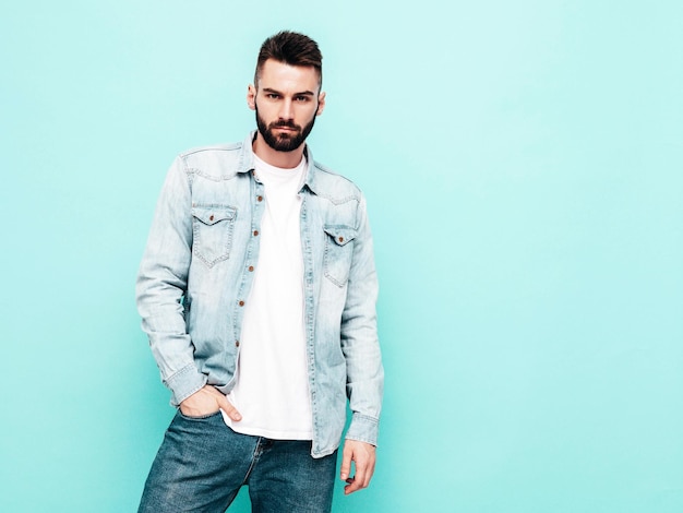 Portrait of handsome confident stylish hipster lambersexual modelMan dressed in jacket and jeans Fashion male isolated on blue wall in studio Thoughtful Isolated