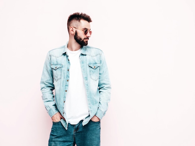 Portrait of handsome confident stylish hipster lambersexual modelMan dressed in jacket and jeans Fashion male posing in studio in sunglasses Isolated