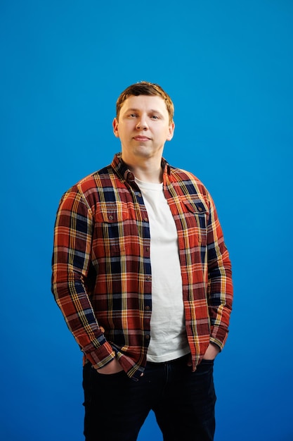 Portrait of handsome european man in shirt looking at camera standing on blue studio background