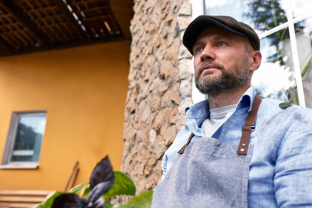 Portrait of handsome gardener wearing hat holds lettuce leaves Organic gardening The concept of harvesting and local farming