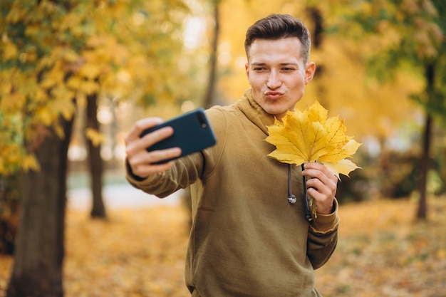 Portrait of handsome guy holding a bouquet of autumn leaves and taking a selfie