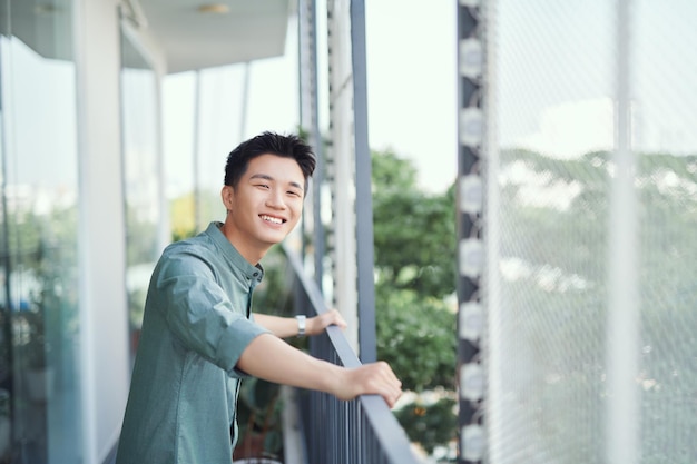 Portrait of handsome guy relaxing on outside balcony isolated on background of buildings and trees