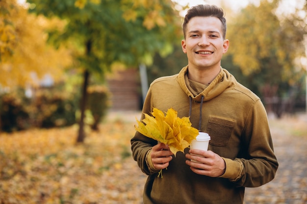 Portrait of handsome guy smiling and holding a bouquet of autumn leaves and cup of coffee