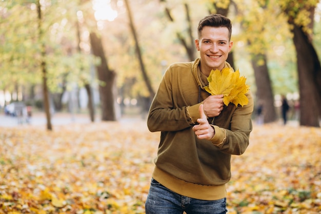 Portrait of handsome guy smiling and holding a bouquet of autumn leaves in the park