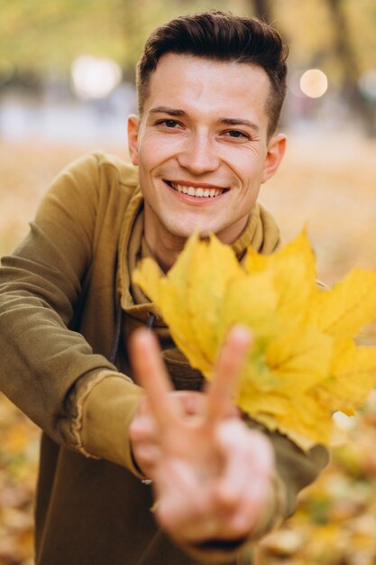 Portrait of handsome guy smiling and holding a bouquet of autumn leaves in the park