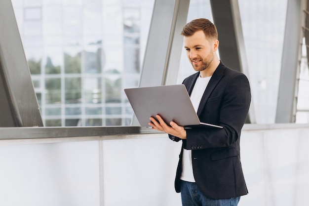 Portrait of handsome happy businessman man in suit holding laptop on background of urban buildings and offices