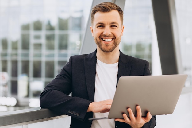 Portrait of handsome happy businessman man in suit holding laptop on background of urban buildings and offices